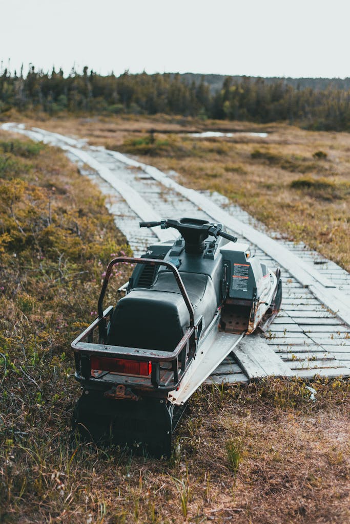 A snowmobile sits on a wooden path in a rustic autumn landscape.